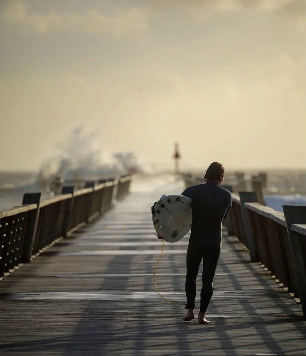Un surfeur remonte l’estacade dans la brume du matin
