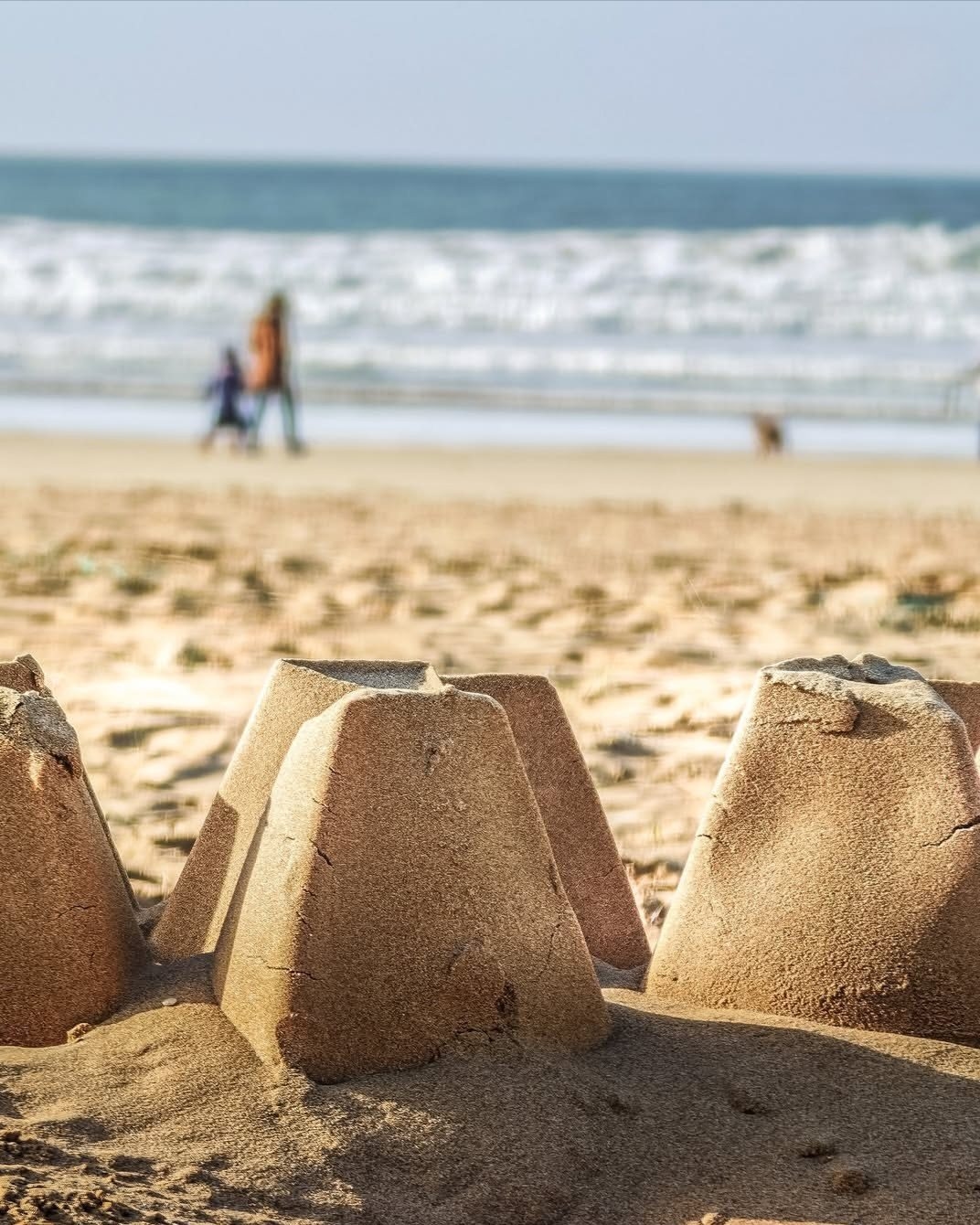 Des pâtés de sable au premier plan, la mer et des promeneurs au loin