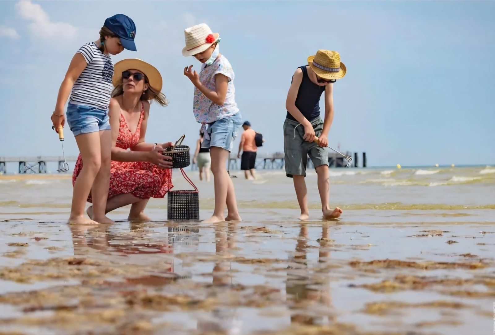 Une mère et ses trois enfants penchés sur un seau, sur le sable mouillé