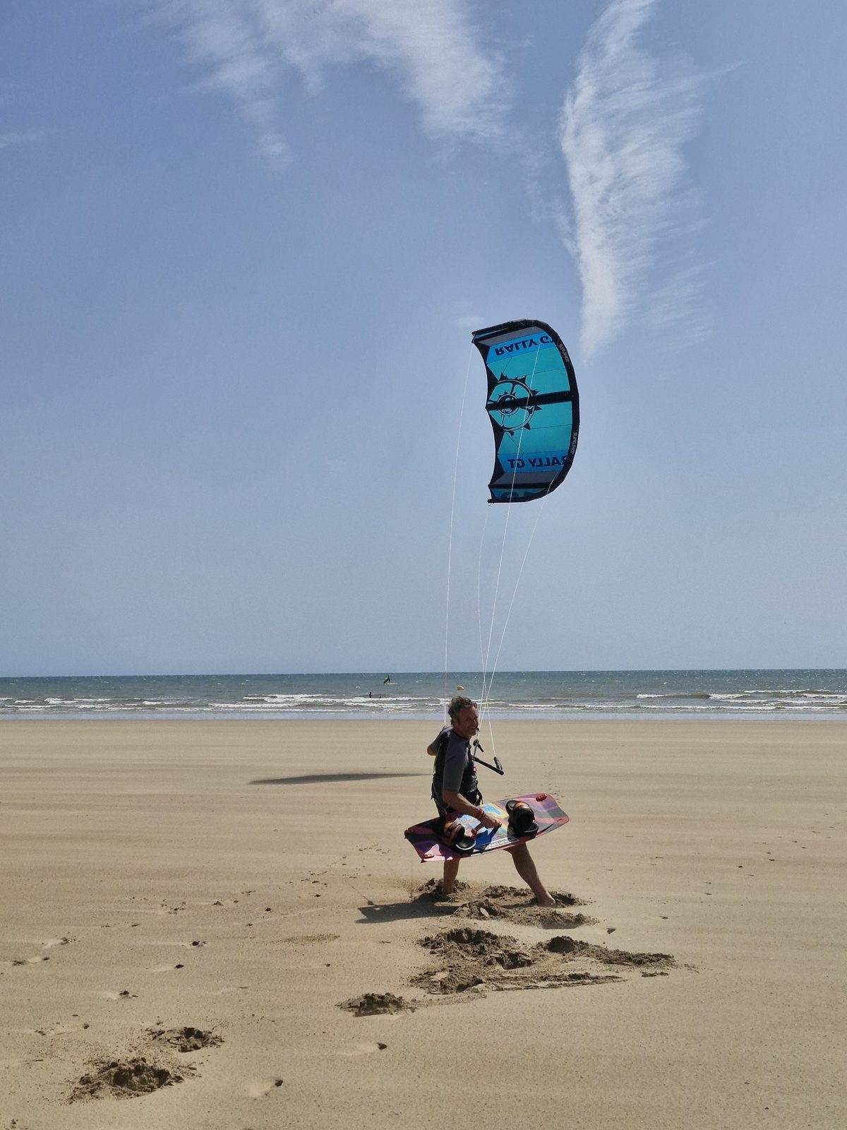 Un kitesurfeur prend son départ sur la plage, l’aile bleue dans le ciel