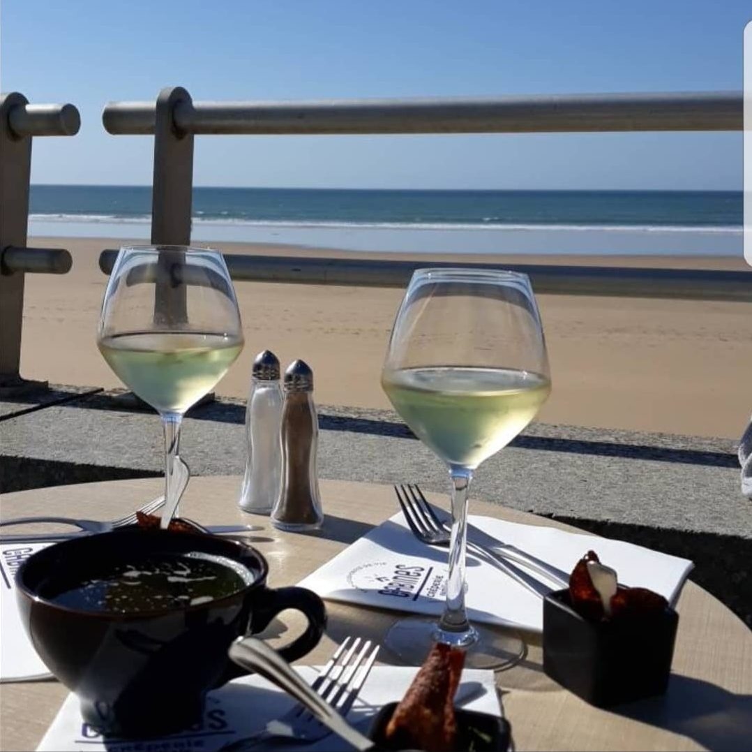 Deux verres de vin blanc sur une table en terrasse, face à la plage