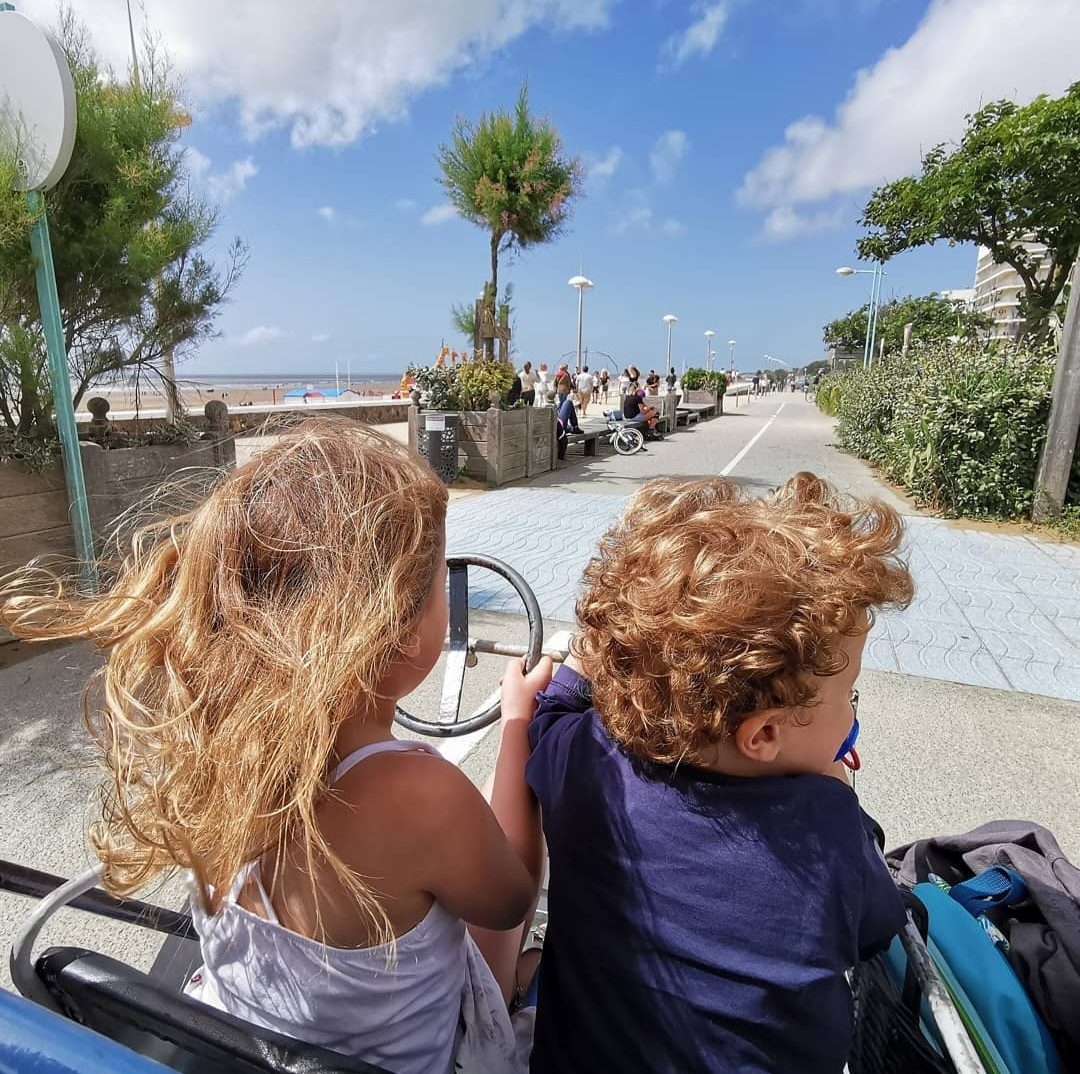 Deux enfants de dos dans une rosalie, sur la promenade du front de mer