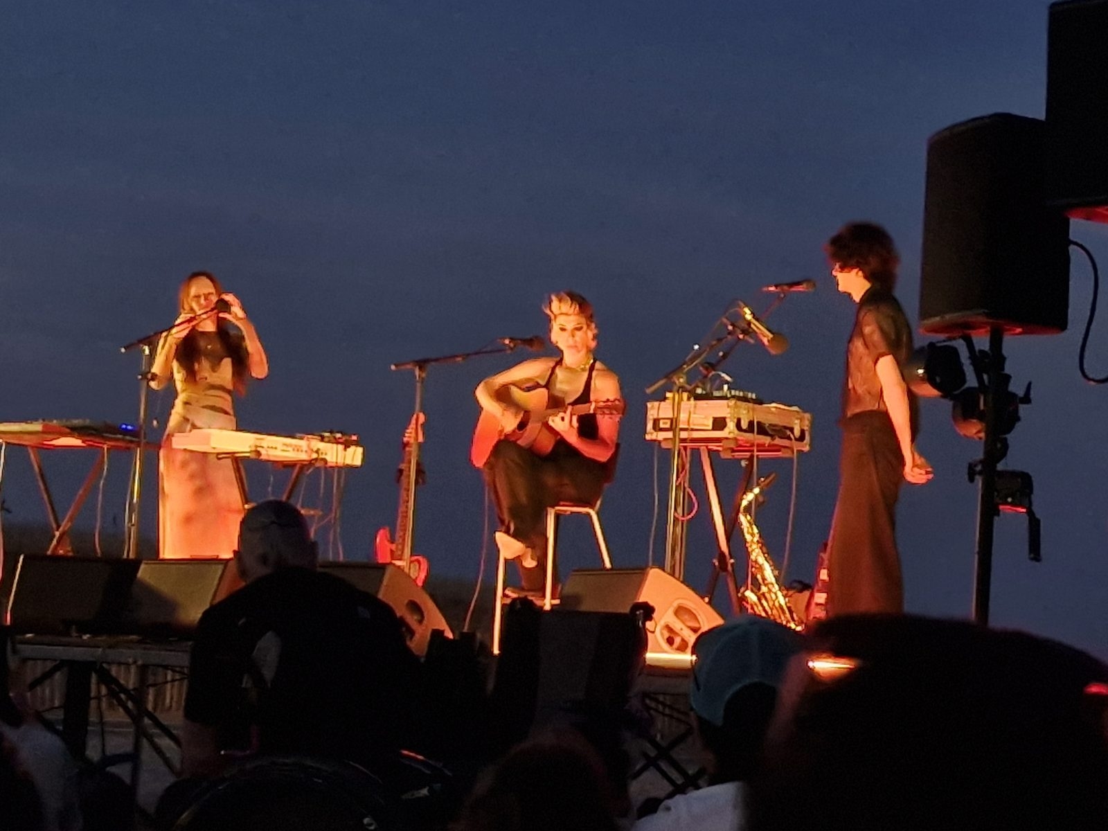 Trois musiciennes sur une scène en plein air, à la tombée de la nuit