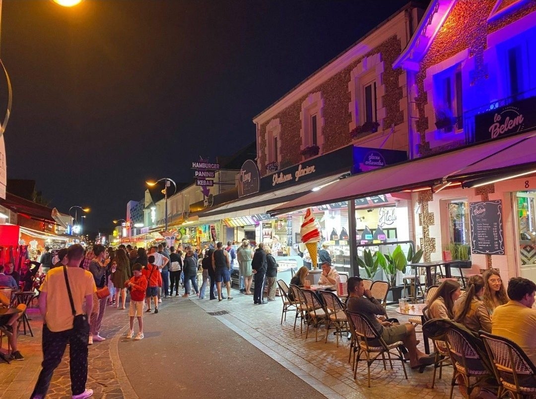 Une rue piétonne animée le soir, terrasses éclairées et promeneurs