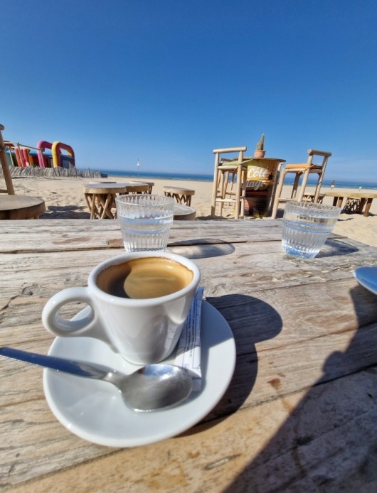 Un café sur une table en bois, face à la plage et à l’océan
